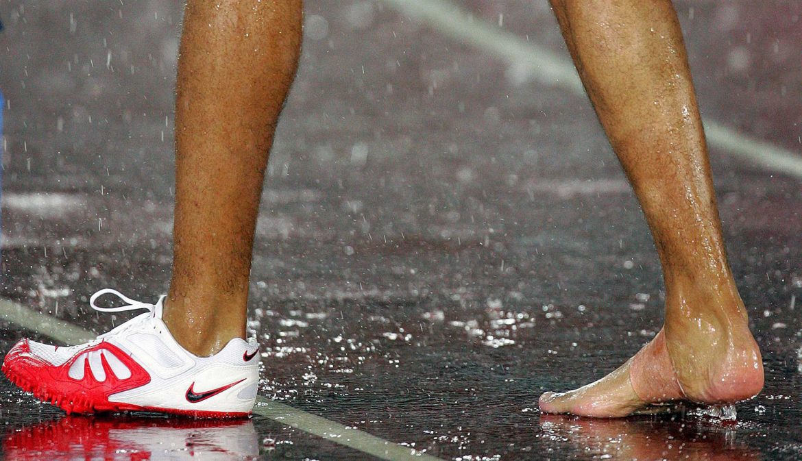 Pie desnudo, junto a la zapatilla deportiva, de un atleta masculino-talones