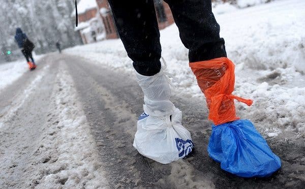 Una mujer se coloca bolsas de plástico sobre sus zapatos para cruzar una calle nevada de Fleet, en Hampshire (Reino Unido). Efesalud.com