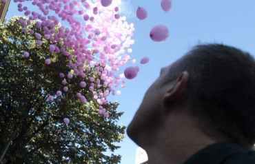 Un hombre mira la los globos rosas que vuelan en el cielo de la ciudad, como símbolo de la lucha contra el cáncer de mama