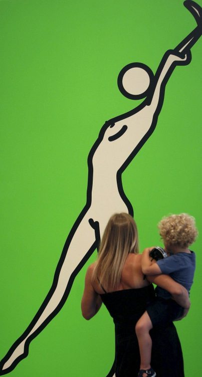 Mujer de espaldas con un niño en brazos observan un cuadro de la silueta estilizada de una mujer sobre fondo verde del artista británico Julian Opie, en el Instituto Valenciano de Arte Moderno (IVAM)