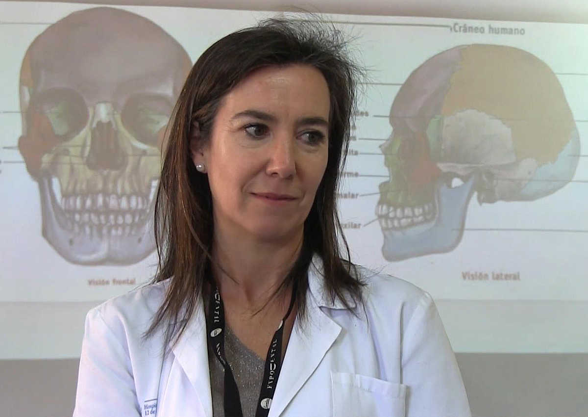 La médico ondontóloga Morales Vera entre dos calaveras que aparecen en una diapositiva proyectada tras ella.