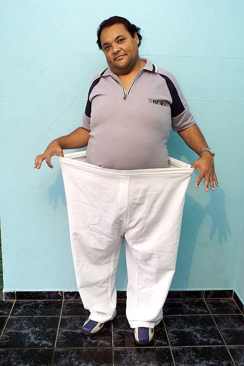 Un joven muestra su pérdida de peso vistiendo un antiguo pantalón en el que ahora caben dos personas