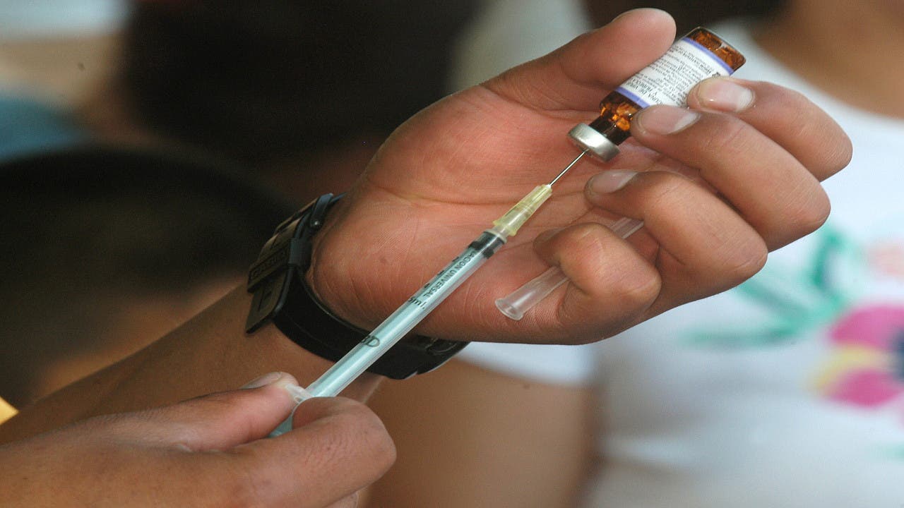 Las manos de un sanitario militar mexicano extraen el fármaco con una inyección contra el virus del sarampión para inocularlo en el brazo de un niño.