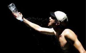 Una persona con gorra y sin camiseta coge al vuelo una botella de agua sobre un fondo negro. Efesalud.com