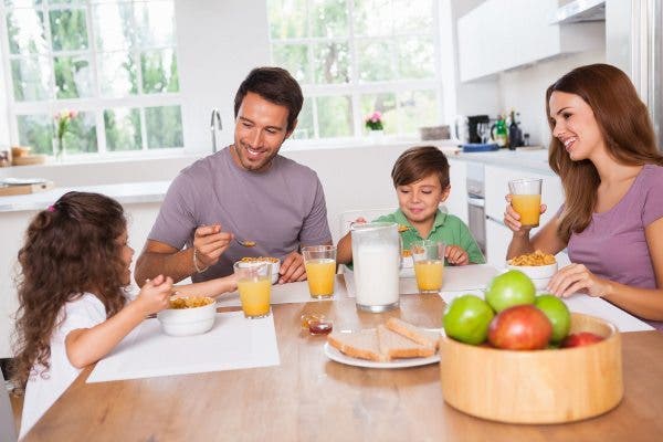 Imagen de una familia con un niño y una niña en una mesa de cocina con productos para el desayuno.