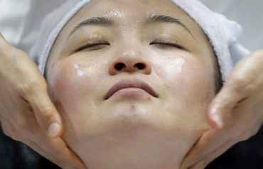 Primer plano del rostro de una mujer asiática que recibe un masaje facial. Efeslaud.com