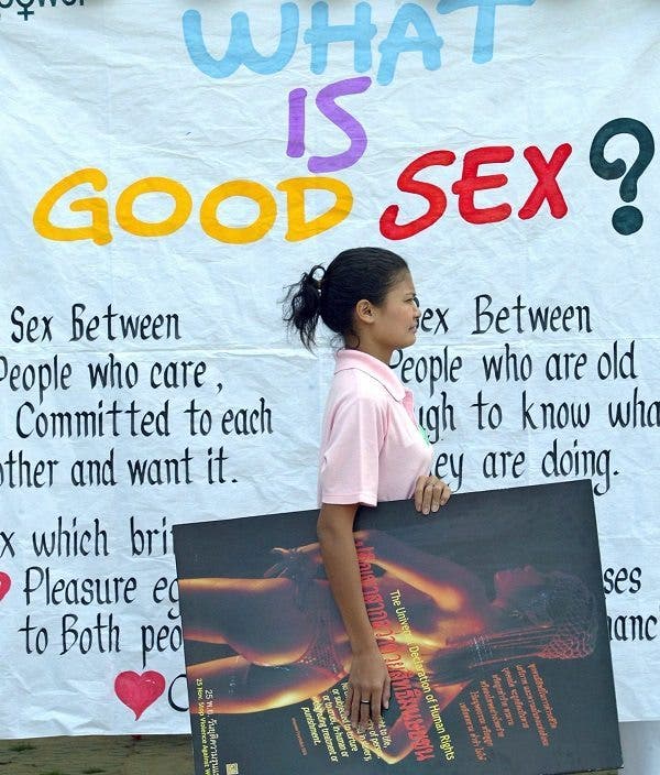 Una mujer tailandesa con un poster de una mujer desnuda en la mano camina delante de una pancarta en la que se lee ¿Qué es buen sexo?' delante del Palacio Real en Bangkok, Tailandia