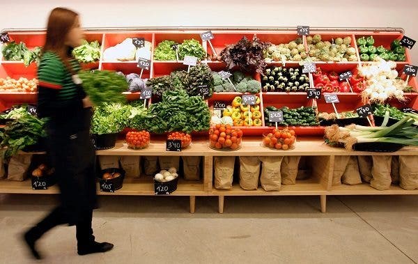 Una trabajadora de un mercado lleva en la mano una lechuga, al fondo las verduras colocadas para su venta. Efesalud.com